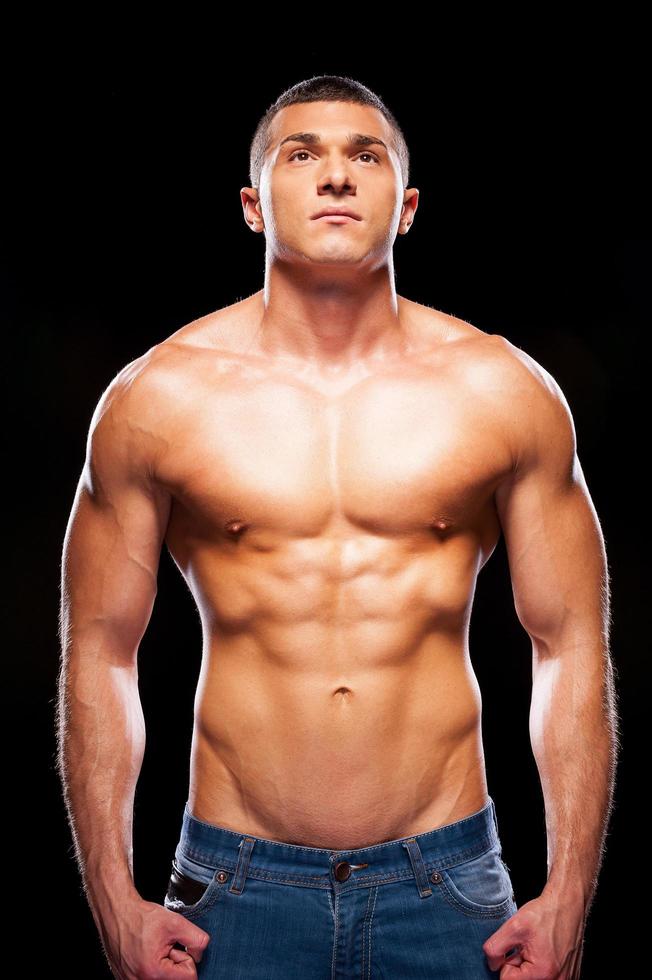 Strong man. Handsome young shirtless man looking up while standing against black background photo