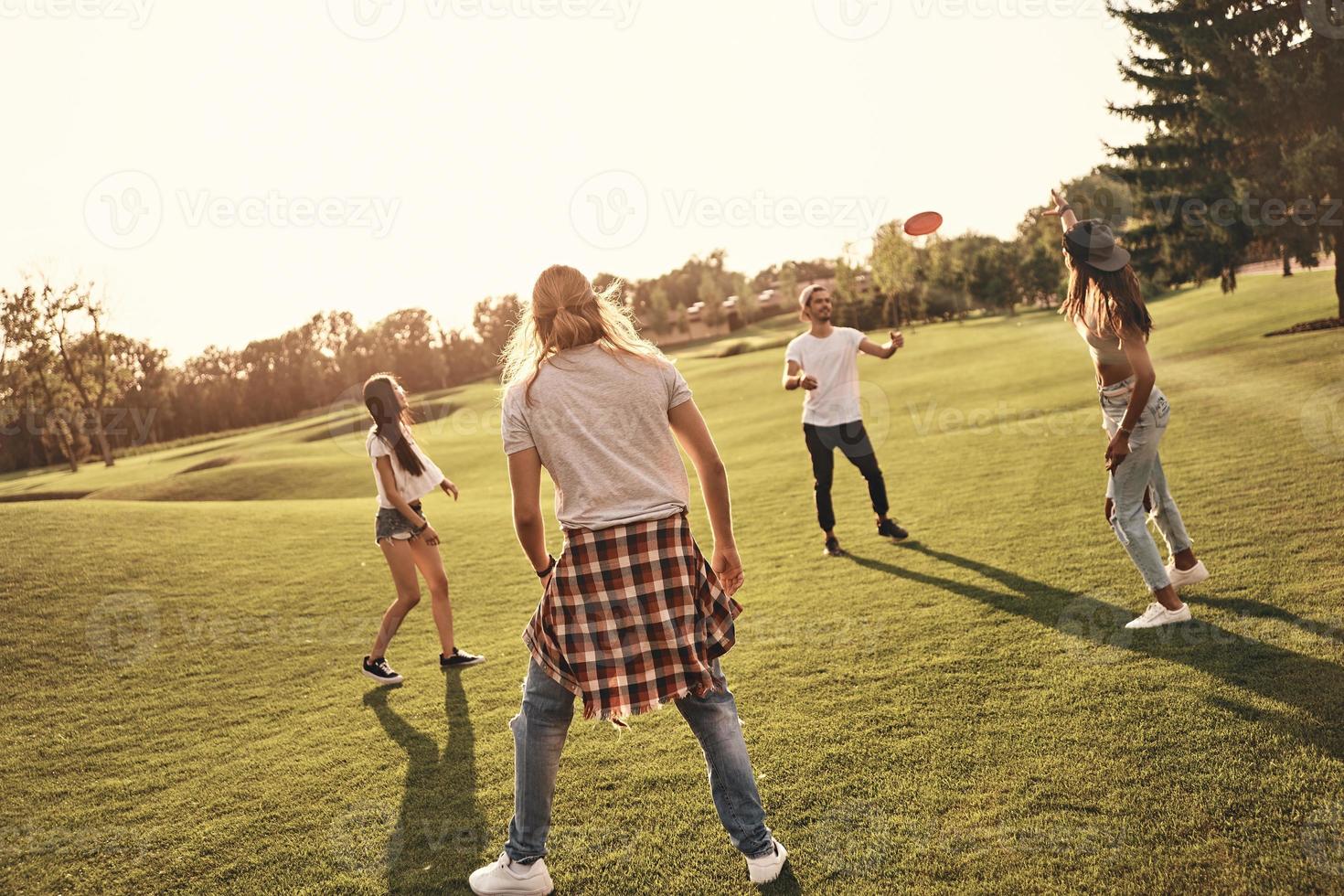 divirtiéndose con amigos. toda la longitud de los jóvenes en ropa casual jugando frisbee mientras pasan tiempo sin preocupaciones al aire libre foto