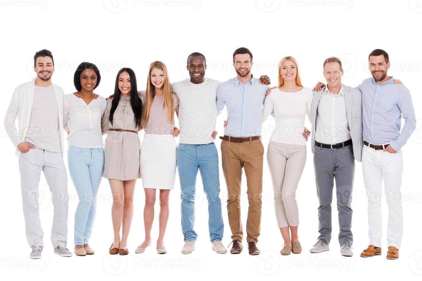 The best team ever. Full length of happy diverse group of people bonding to each other and smiling while standing against white background together photo