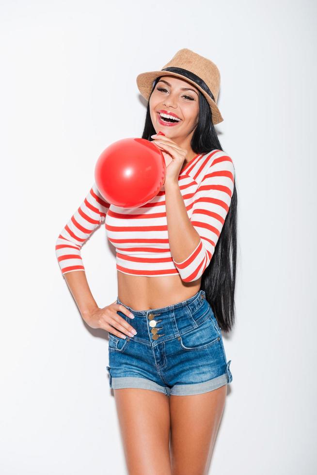 Balloon fun. Joyful young woman holding red balloon while standing against white background photo