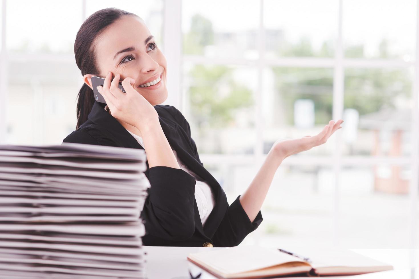 Confident and successful. Happy young woman in formalwear talking on the mobile phone while sitting at her working place photo