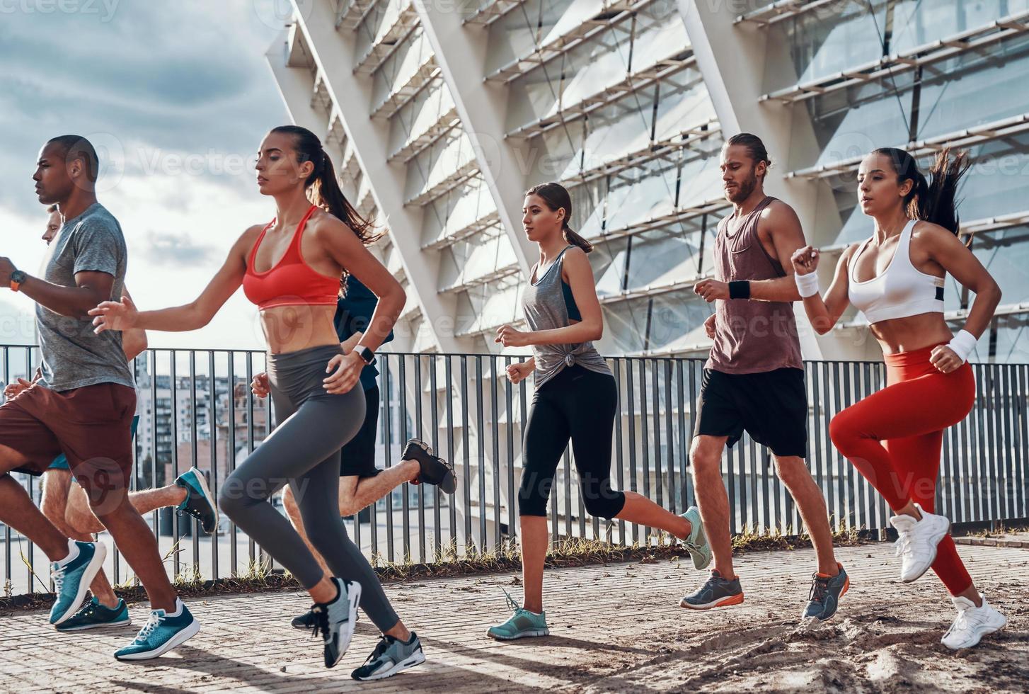 toda la longitud de los jóvenes en ropa deportiva trotando mientras hacen ejercicio al aire libre foto