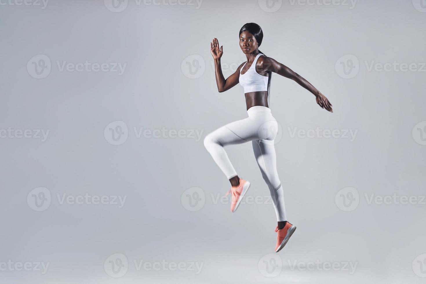 Full length of confident young African woman in sports clothing jumping against gray background photo