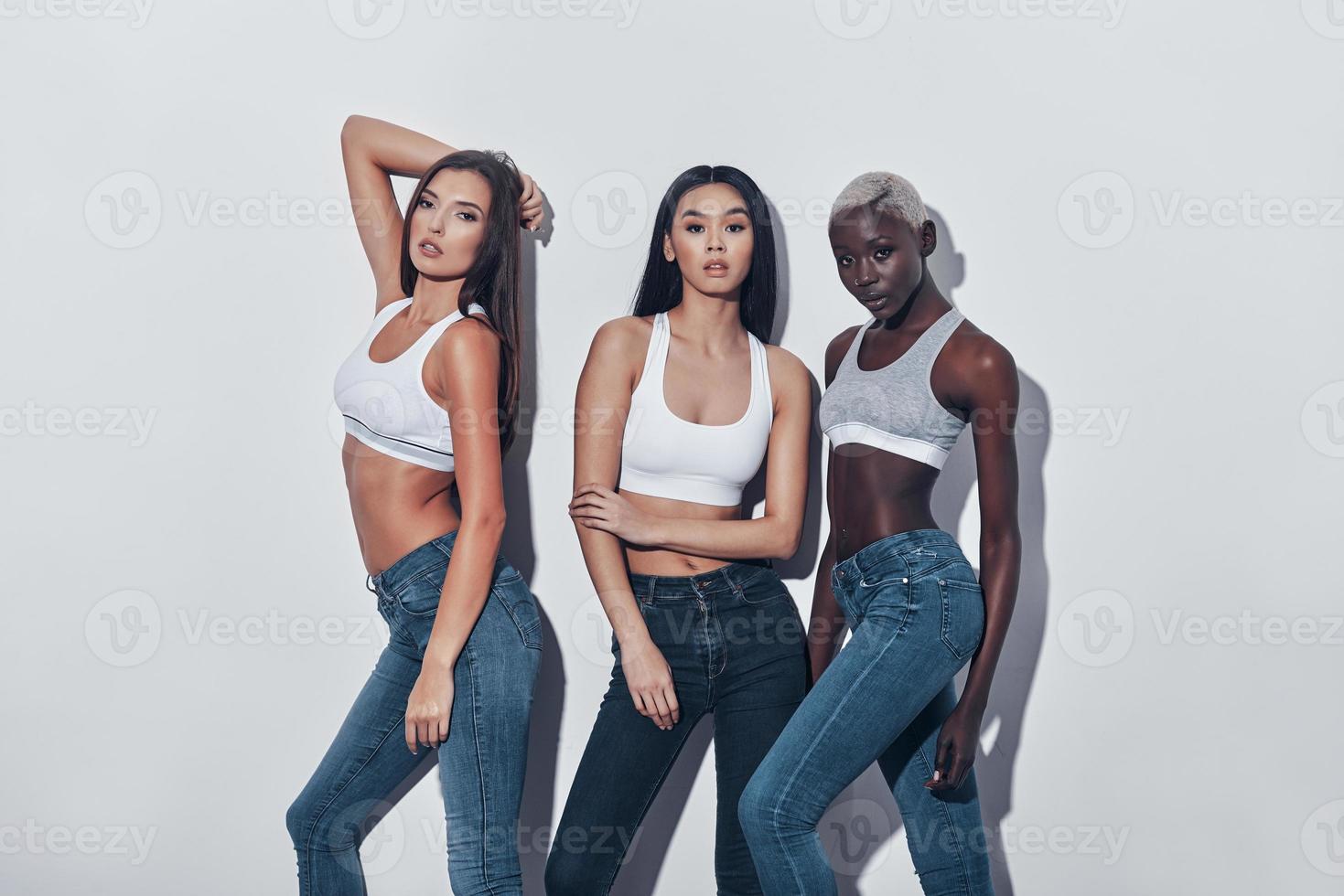 Impossible to resist their beauty. Three attractive young women looking at camera while standing against grey background photo