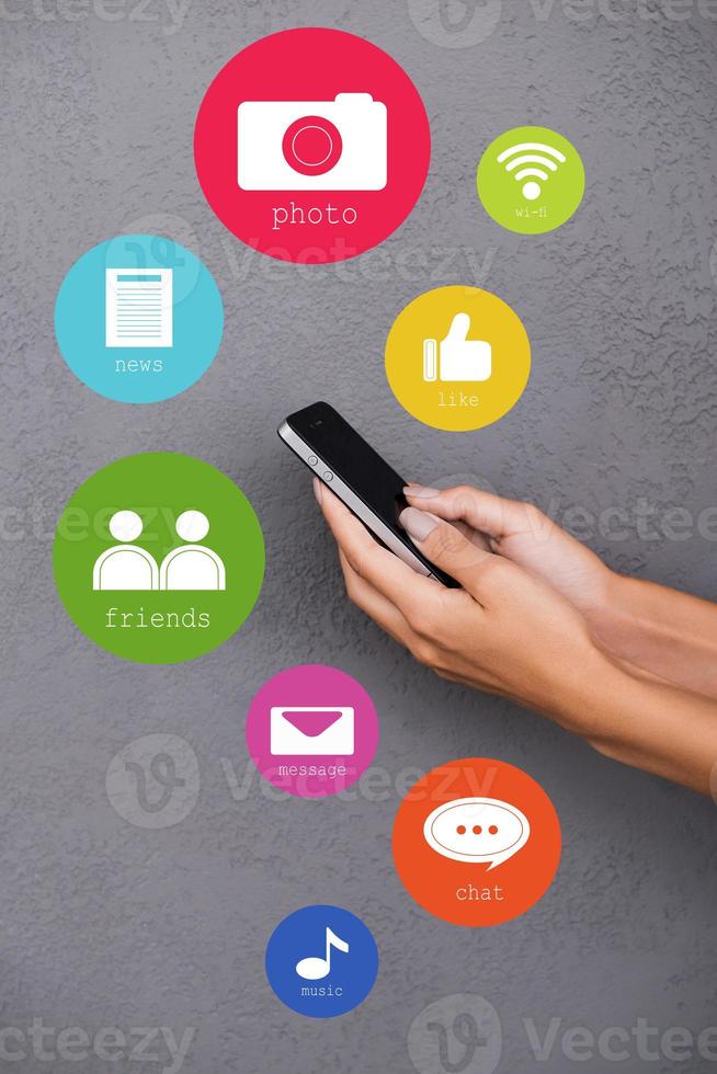 Staying connected. Close-up of female hands holding smart phone with colorful vector icons around it photo