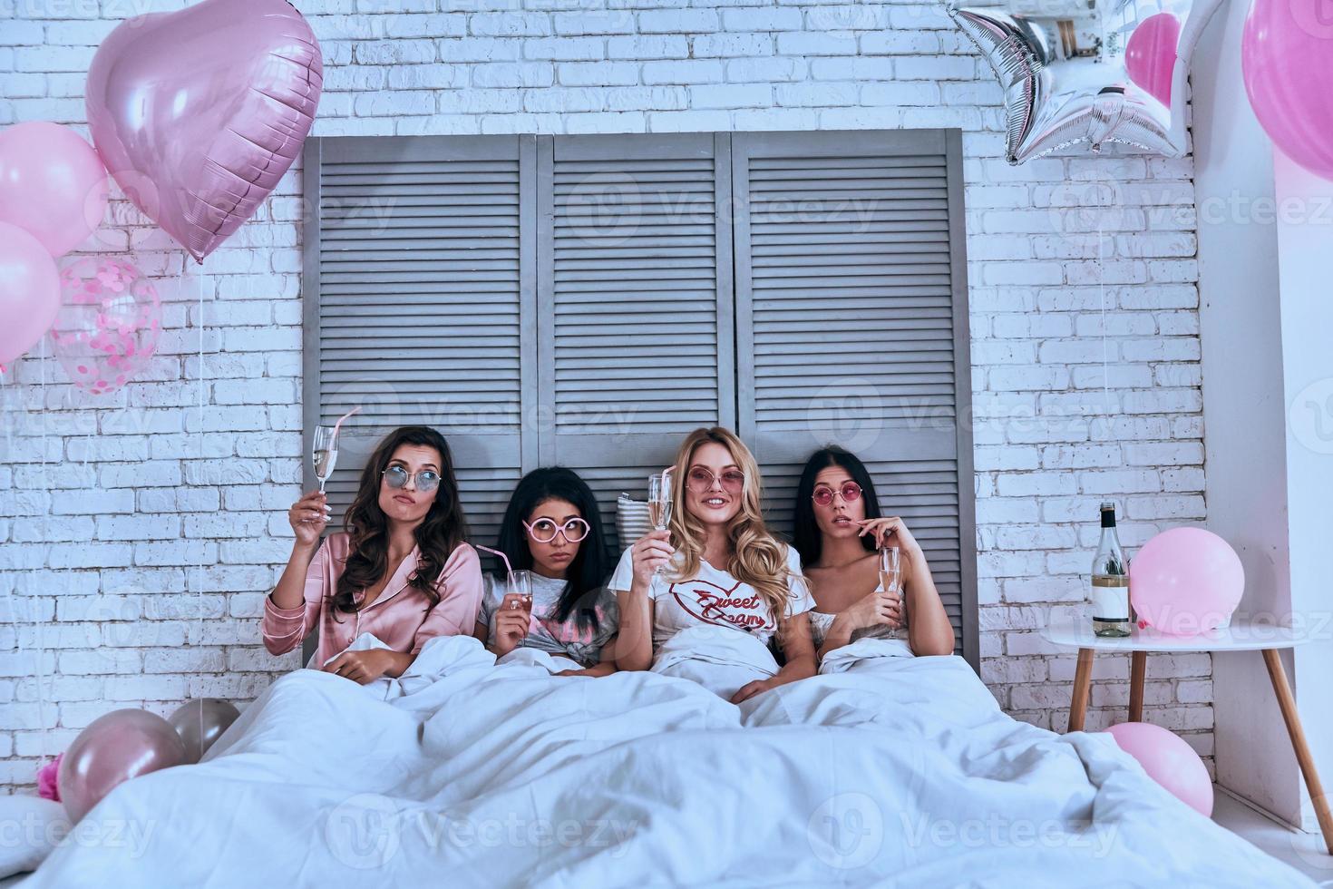 So much fun Four attractive young women in pajamas drinking cocktails while lying in the bed with balloons all over the room photo