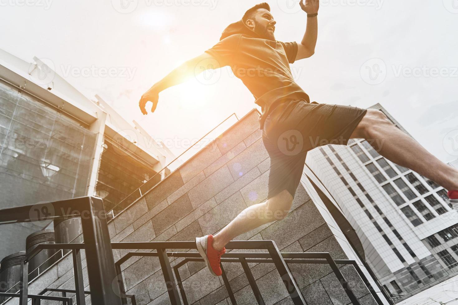 On the move. Low angle view of handsome young man in sport clothing jumping while exercising outside photo