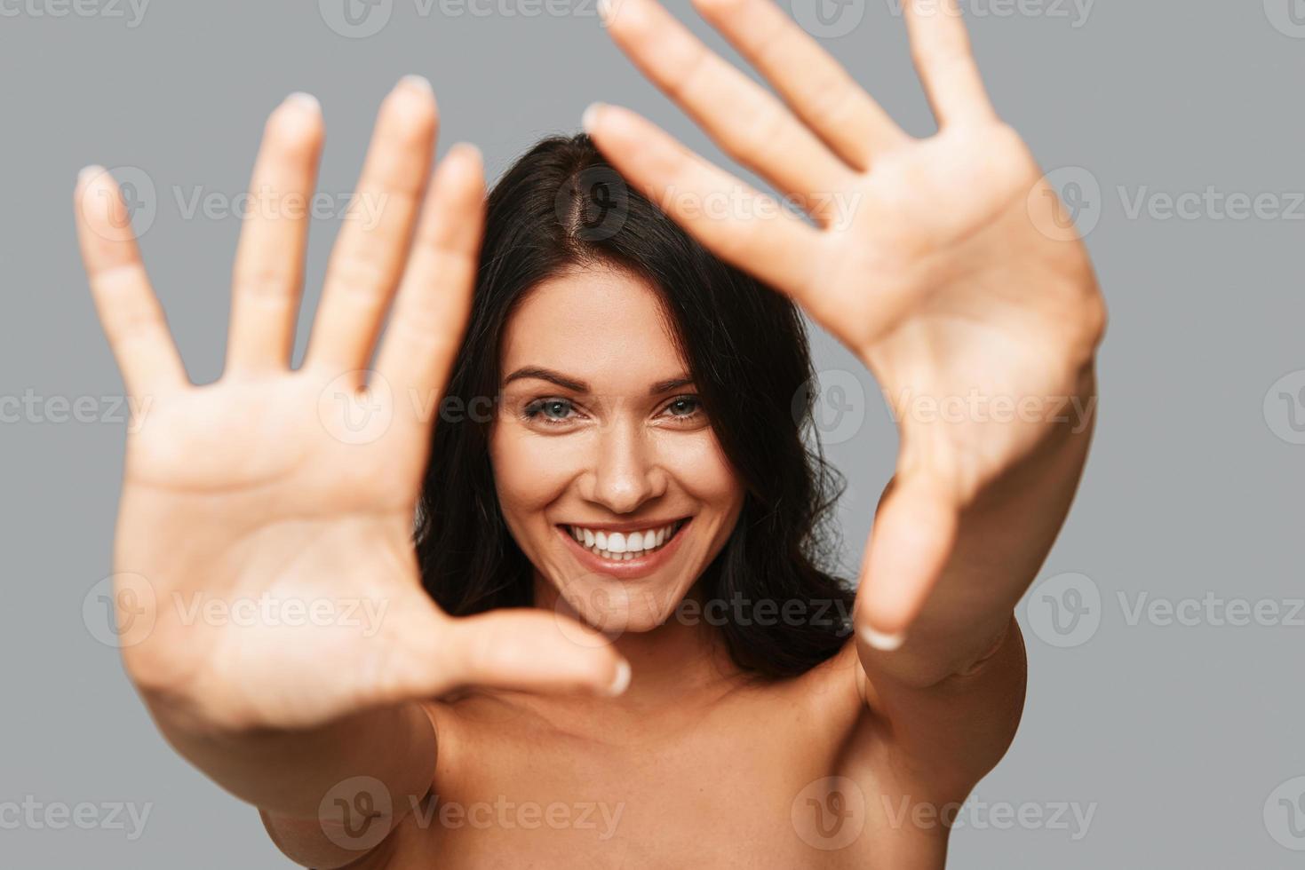 Beauty in focus Beautiful young woman looking at camera and gesturing while standing against grey background photo
