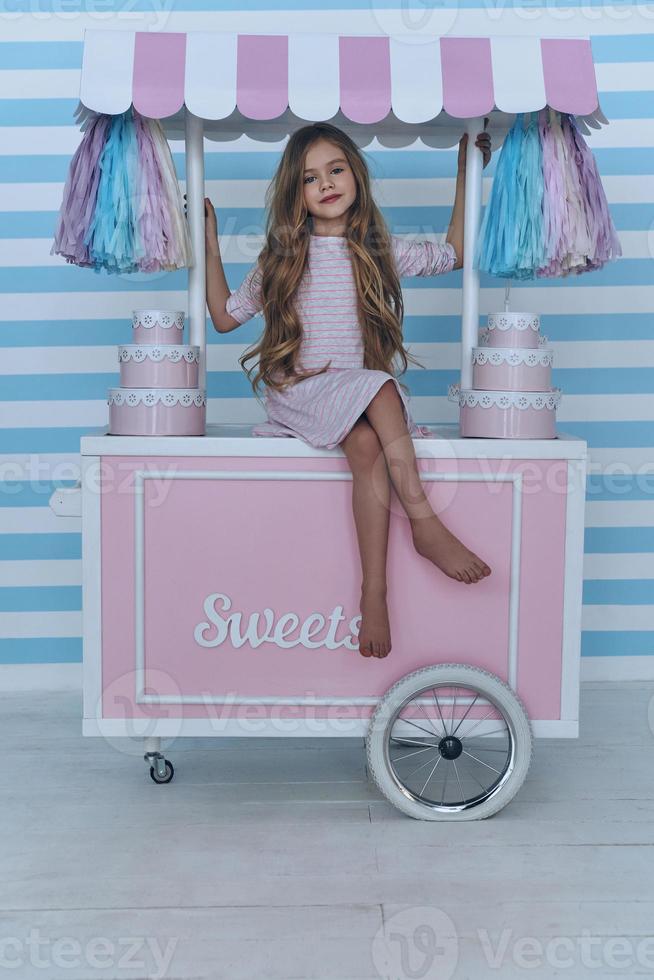 Ready to sell candies.  Cute little girl looking at camera and smiling while sitting on the candy cart decoration photo