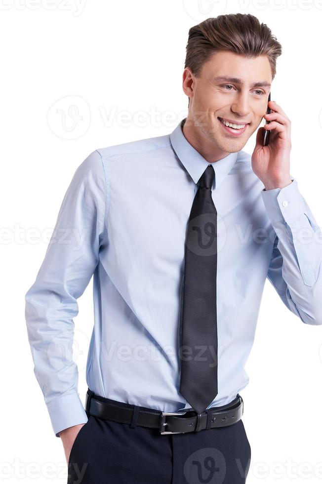 Great news Handsome young man in formalwear talking on the mobile phone and smiling while standing isolated on white photo