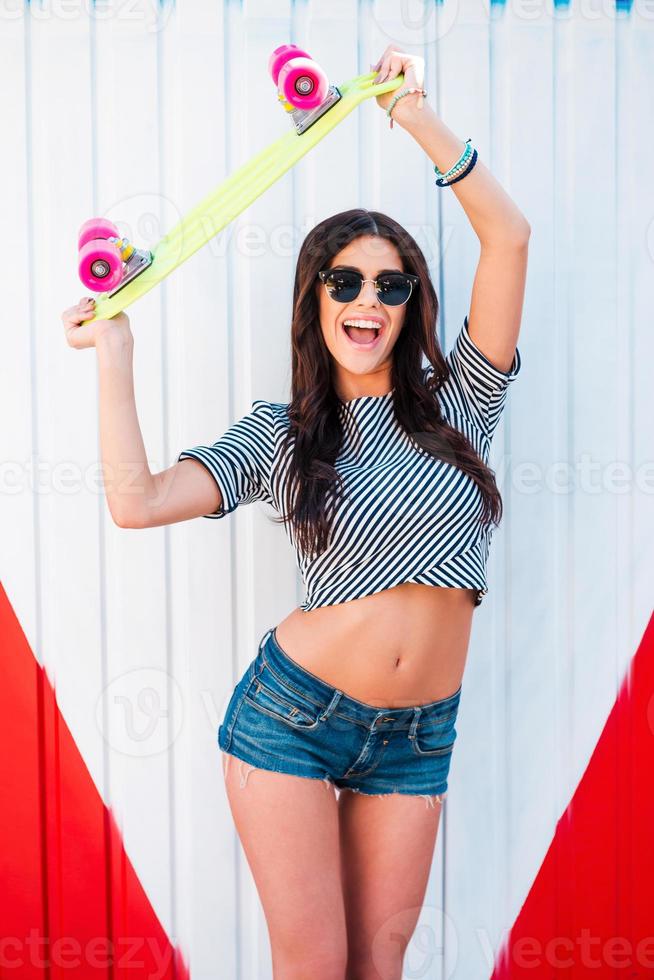 The best city transport Cheerful young women holding skateboard under her head and smiling while standing against colorful background photo