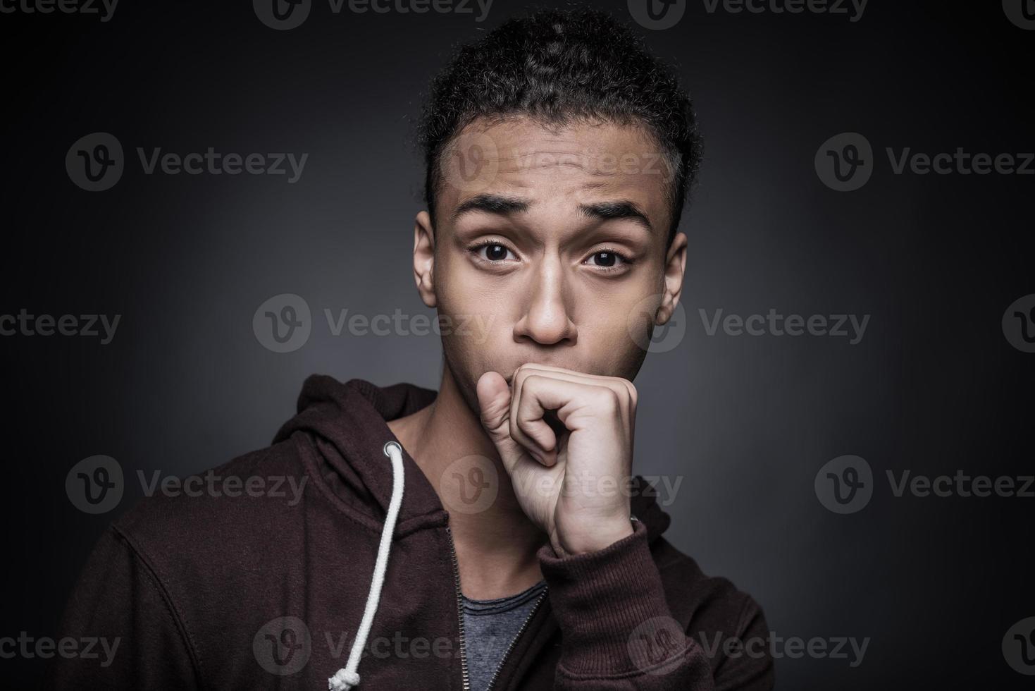 Come on Portrait of young African man looking at camera and covering his mouth with fist while standing against black background photo