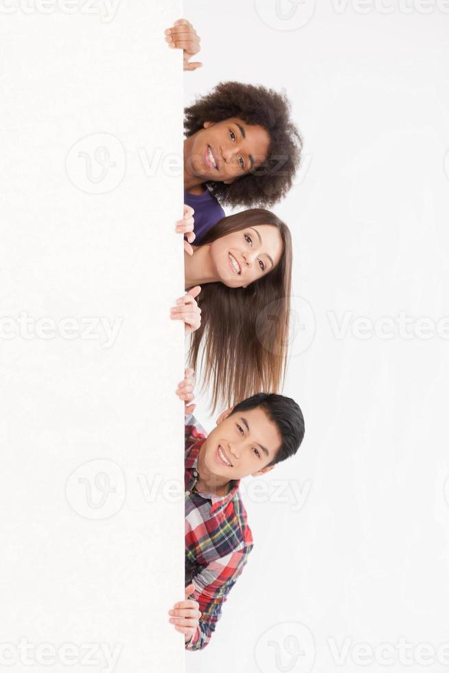 Hello Cheerful young multi-ethnic people looking out of copy space and smiling at camera while isolated on white photo