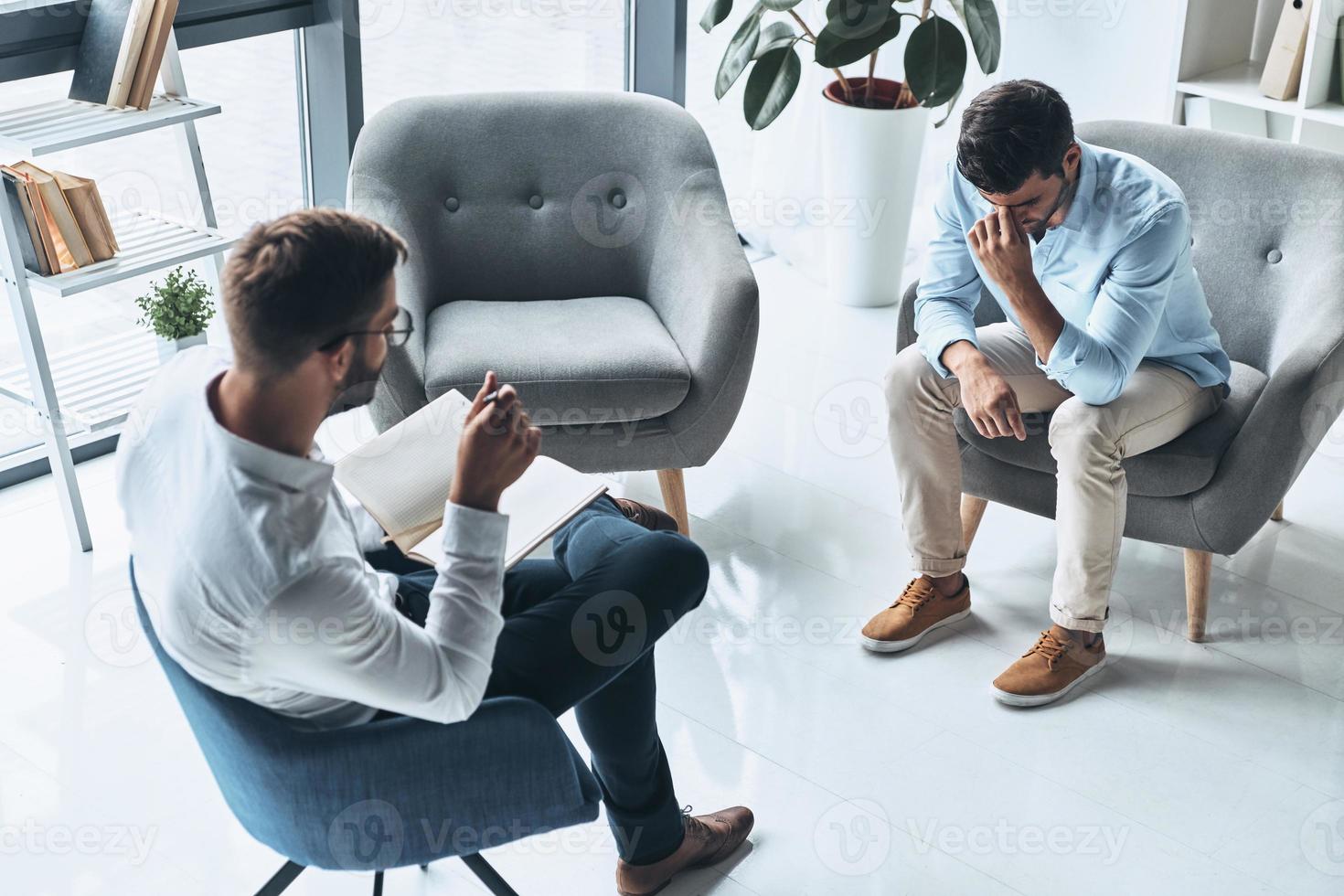 Totally despaired. Top view of young frustrated man solving his mental problems while having therapy session with psychologist photo