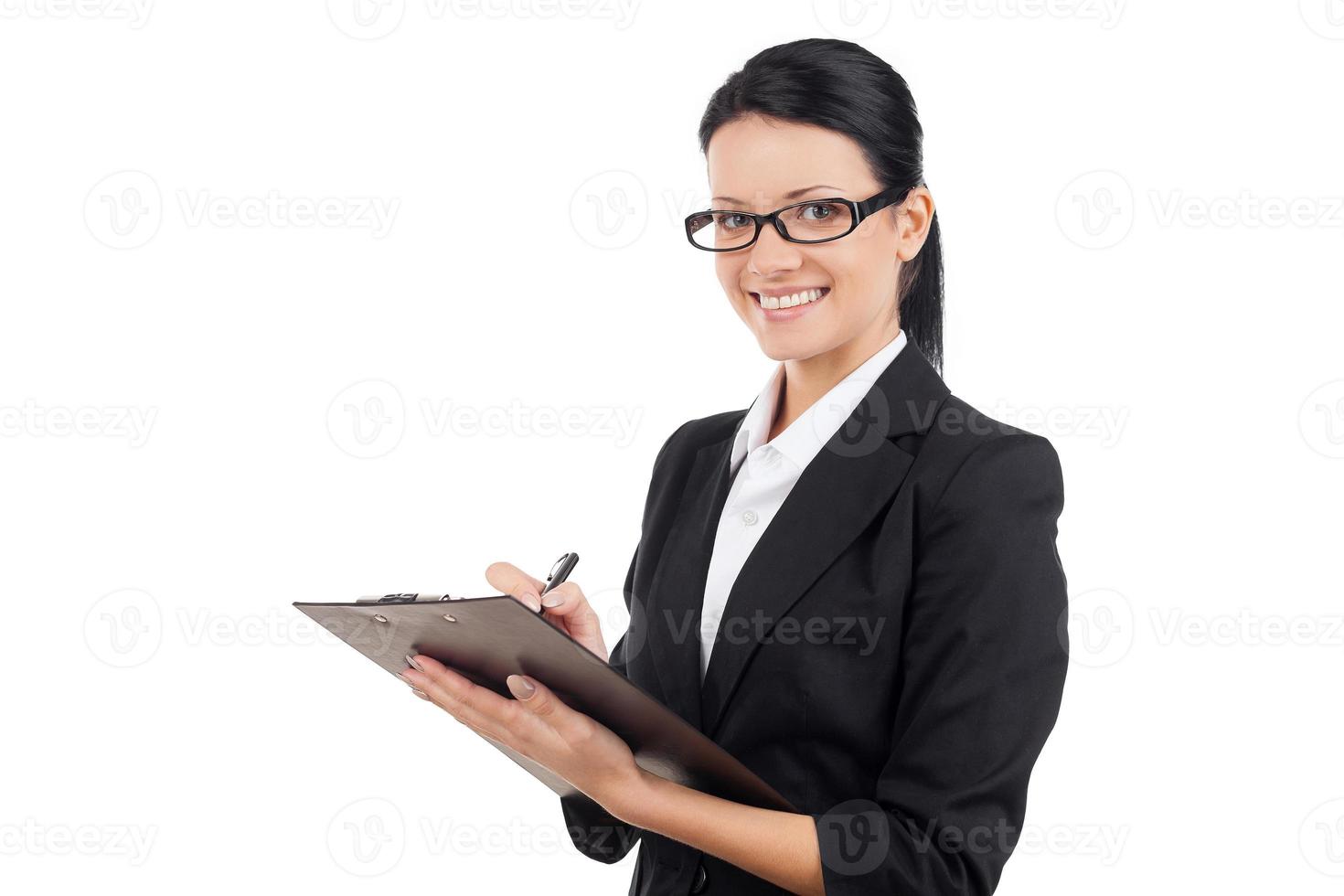 Cheerful businesswoman. Cheerful young business woman writing something in her note pad and smiling at camera while standing isolated on white photo