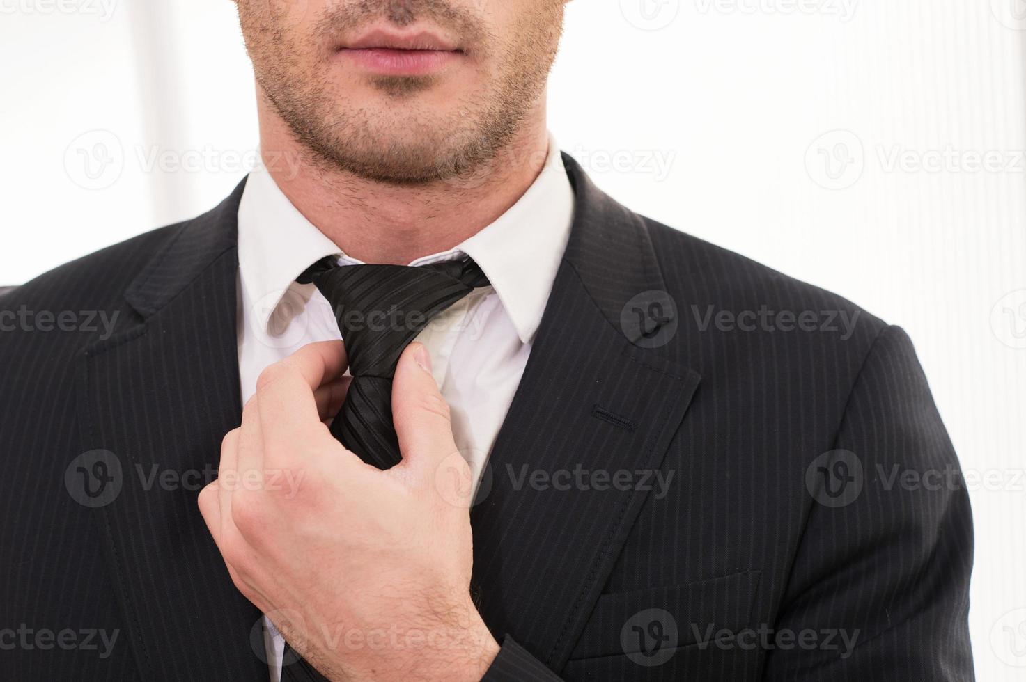 Good looking business. Cropped image of young man in formalwear adjusting his necktie photo