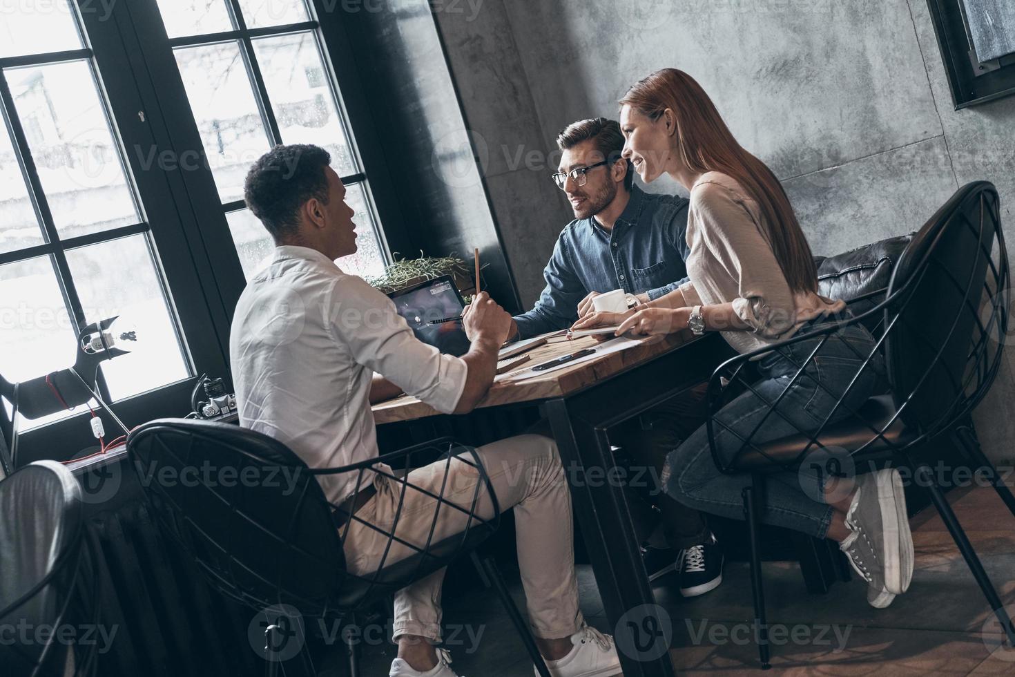 Group of young modern people in smart casual wear discussing something while working in office photo
