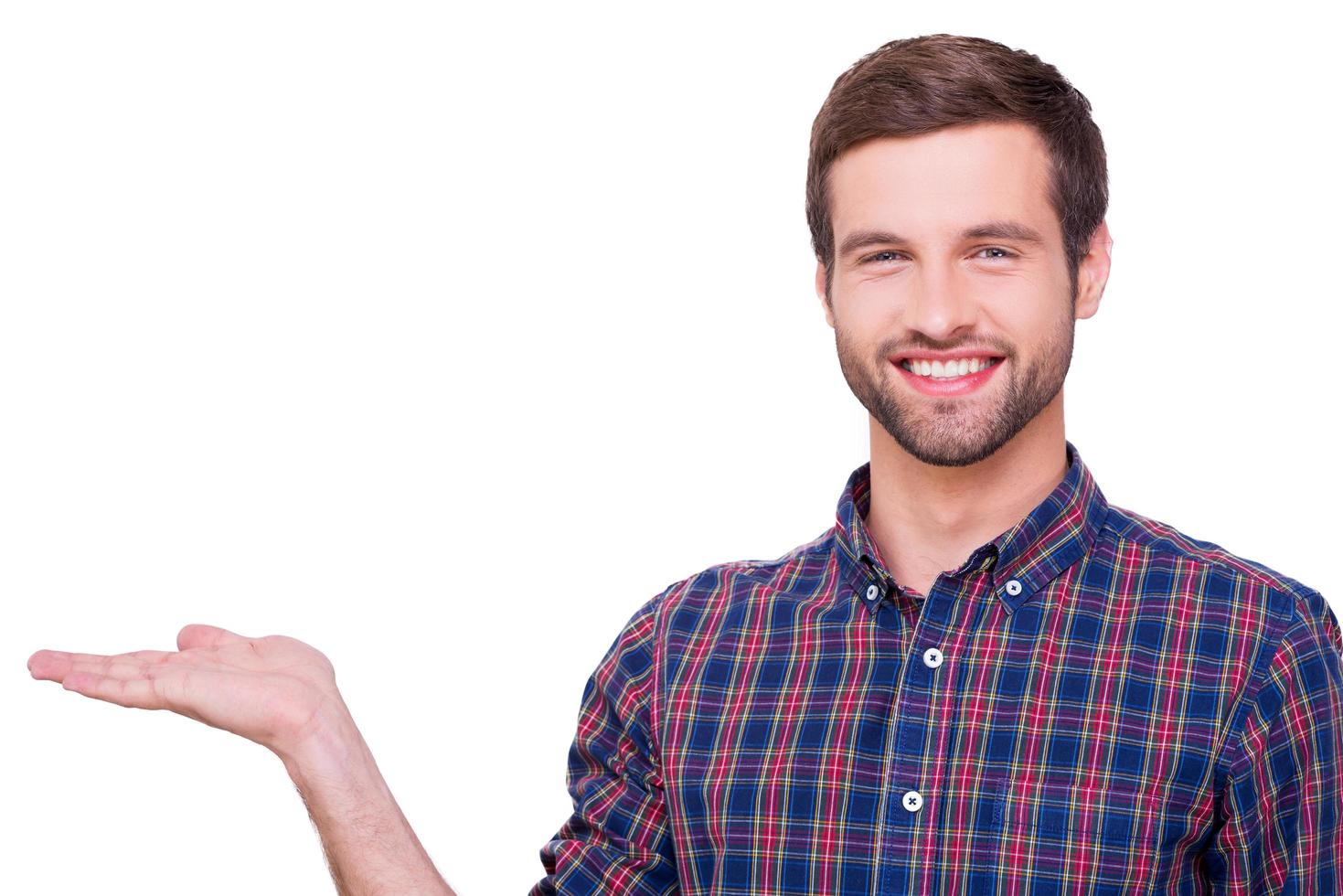 Copy space in his hand. Portrait of handsome young man in casual shirt holding copy space and looking at camera with smile while standing isolated on white photo