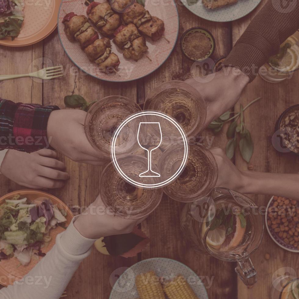 Digitally composed picture of wine glass over top view of four people cheering with red wine while sitting at the rustic dining table photo