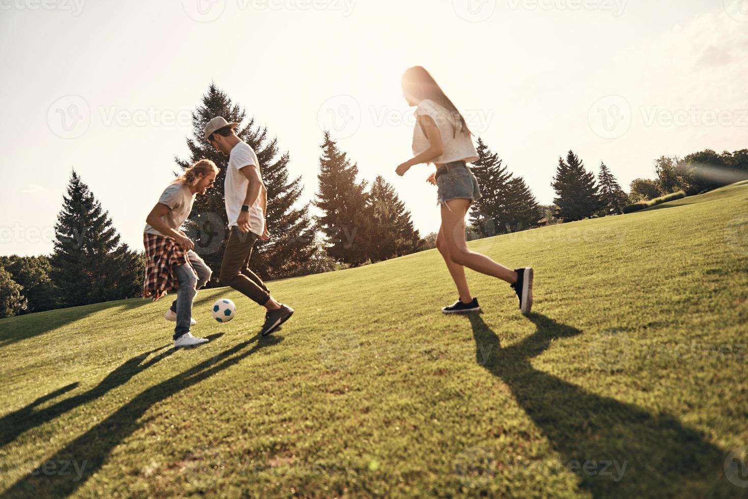 Feeling playful. Full length of happy young people in casual wear playing soccer while running outdoors photo