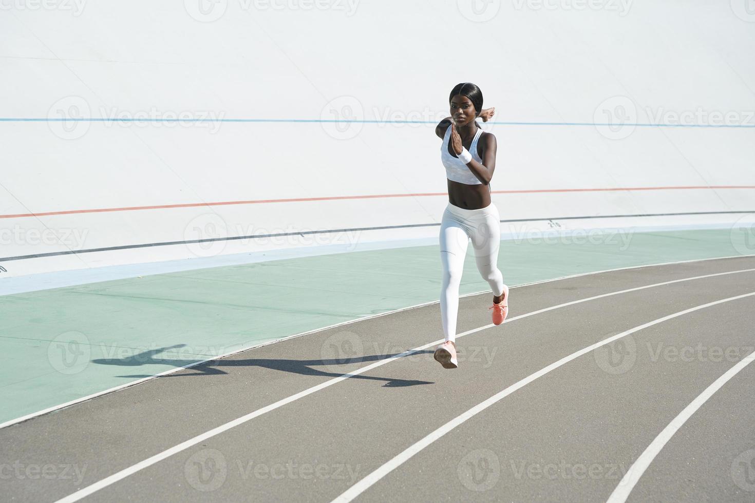 Beautiful young African woman in sports clothing running on track outdoors photo
