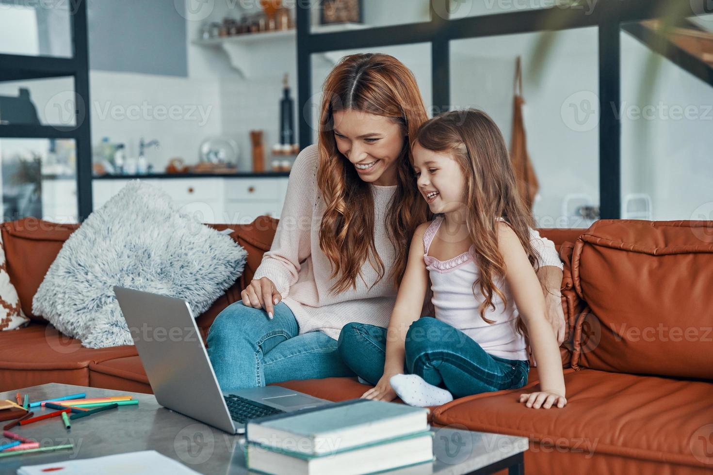 Loving beautiful mother and her little daughter bonding together and smiling while using laptop at home photo