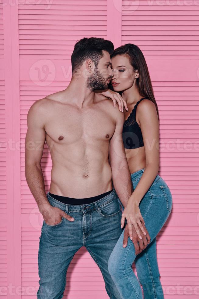 pareja perfecta. hermosa joven pareja abrazándose mientras está de pie contra el fondo rosa foto