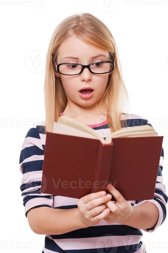 No way Surprised little girl reading book and keeping mouth open while standing isolated on white photo