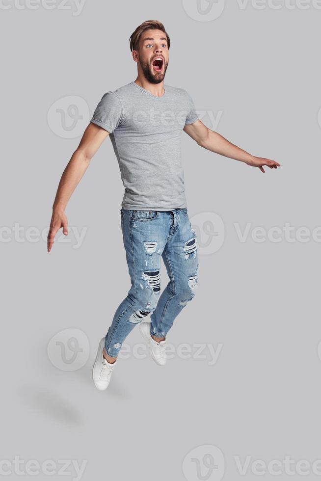 Going crazy. Full length of handsome young man shouting while jumping against grey background photo