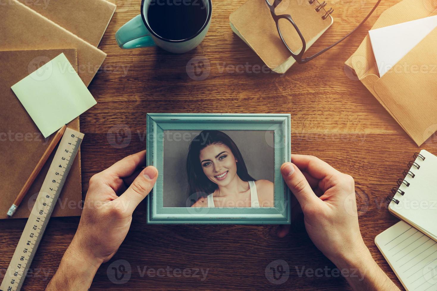 My wife is my inspiration. Close-up top view of man holding photograph of beautiful young woman over wooden desk with different chancellery stuff laying around photo