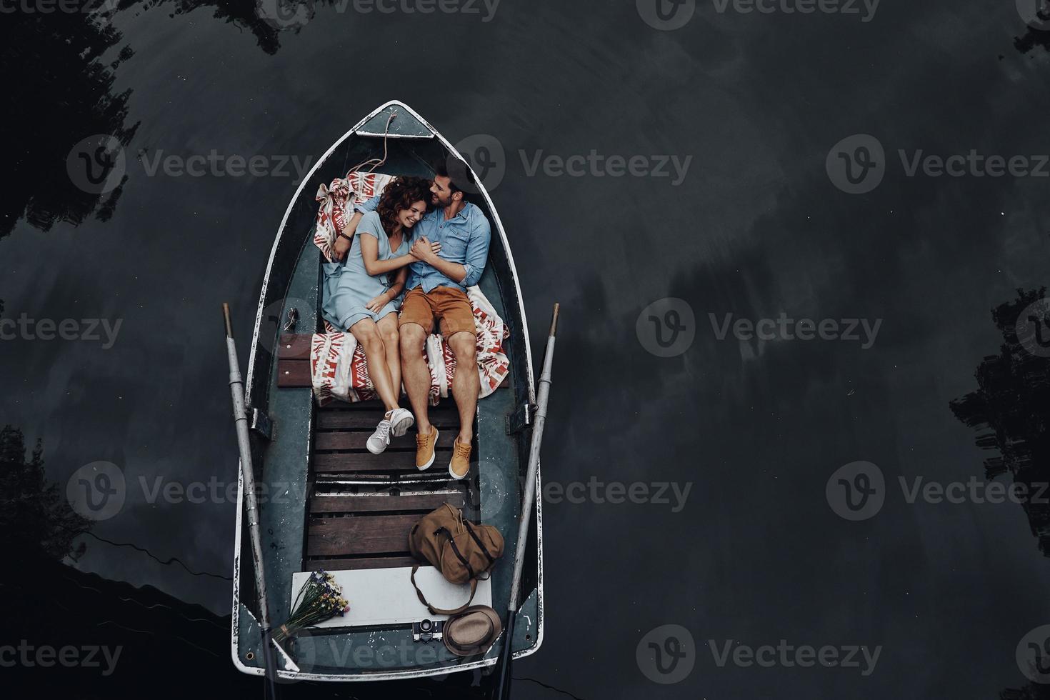 Loving couple in boat. Top view of beautiful young couple embracing and smiling while lying in the boat photo