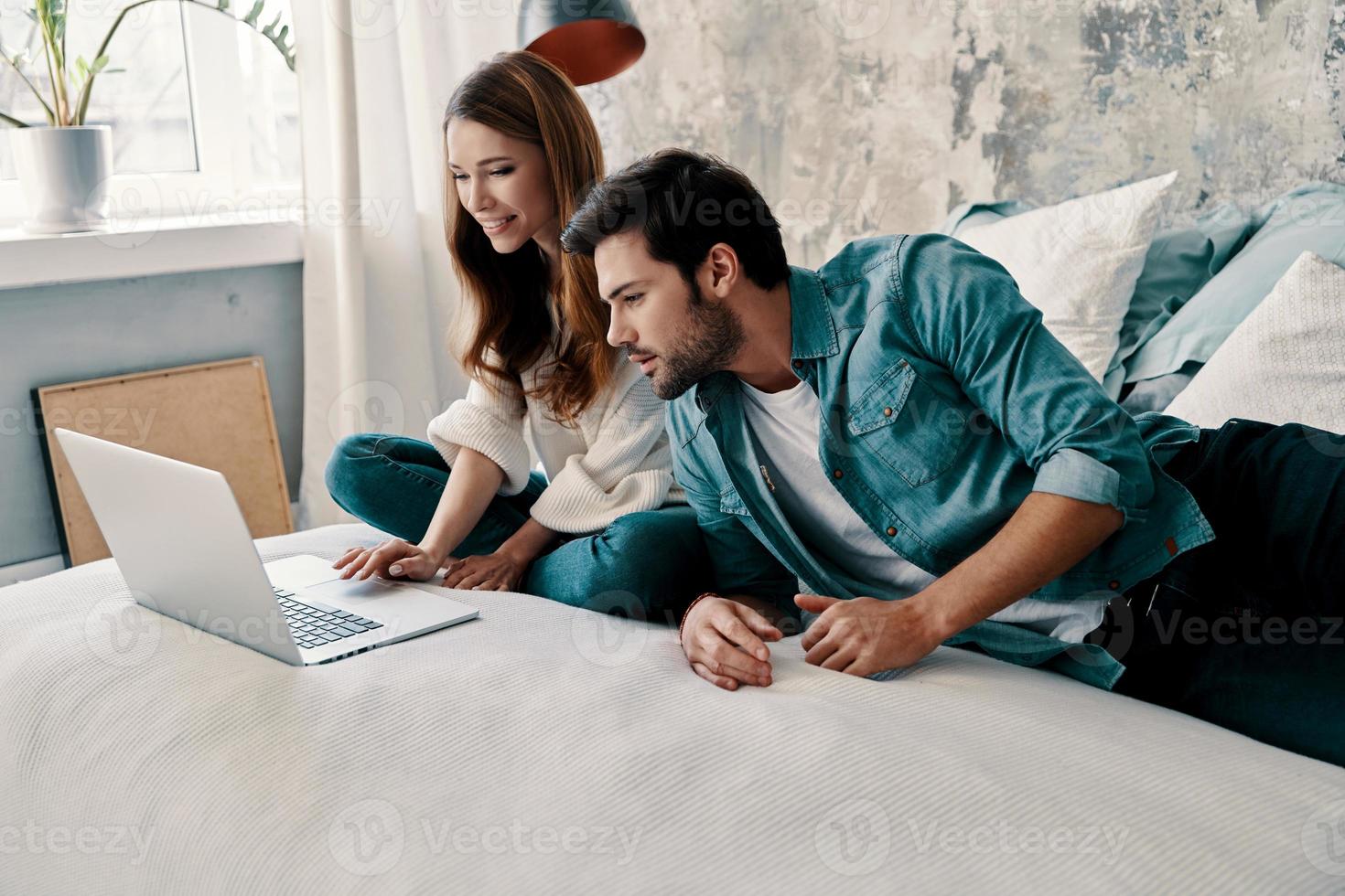 Surfing the net. Beautiful young couple using computer while spending time in bed at home photo