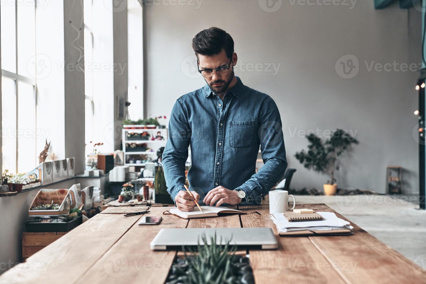 concentración total. joven pensativo escribiendo algo mientras trabaja en el espacio de trabajo creativo foto