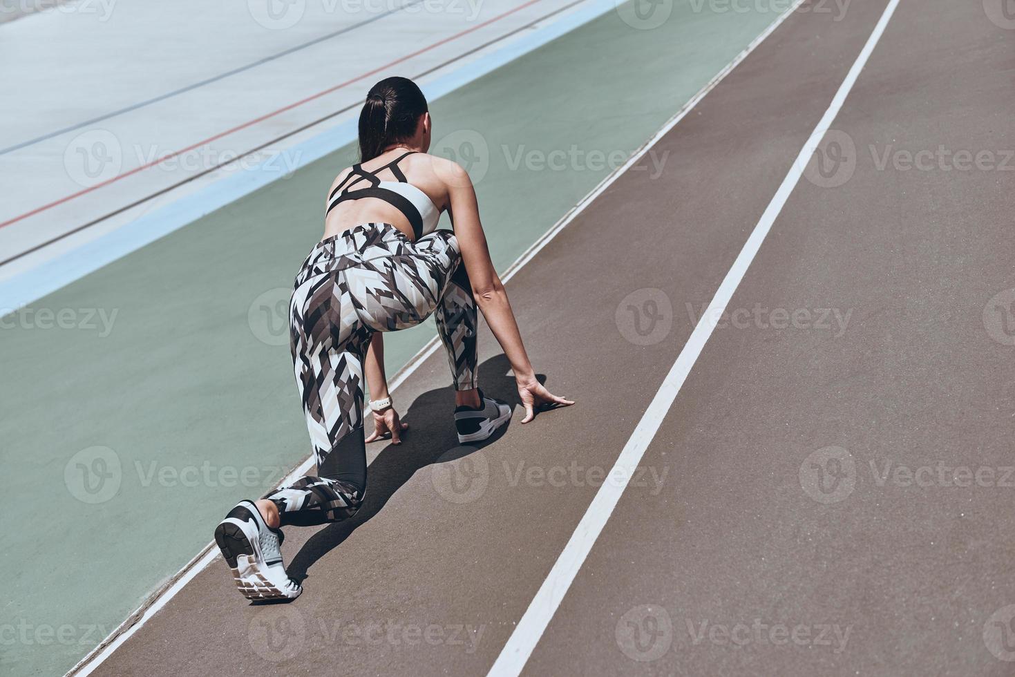 Pushing hard. Top rear view of young woman in sports clothing standing on the start line while running outdoors photo