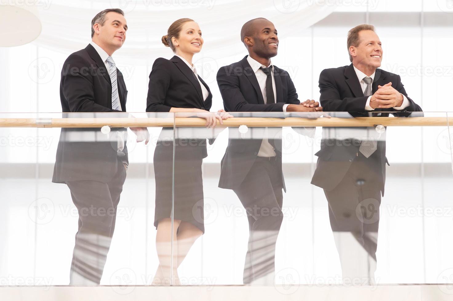 Business team. Low angle view of four cheerful business people standing close to each other and looking away photo