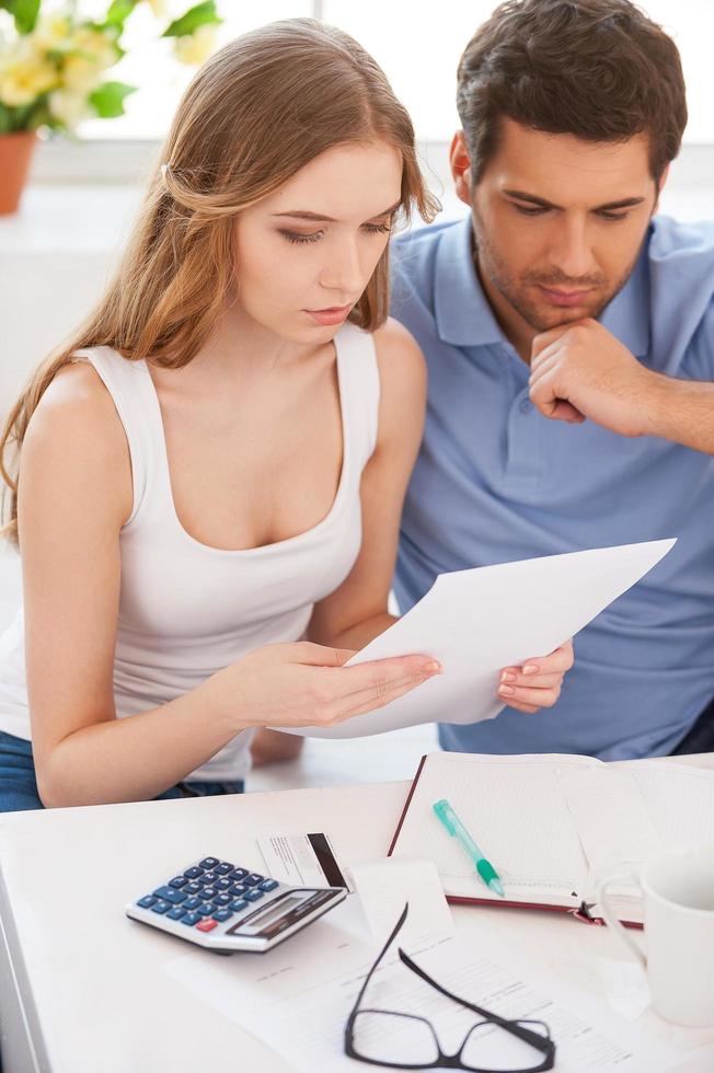 Finding out solution. Top view of thoughtful young couple reading document while sitting close to each other at their apartment photo