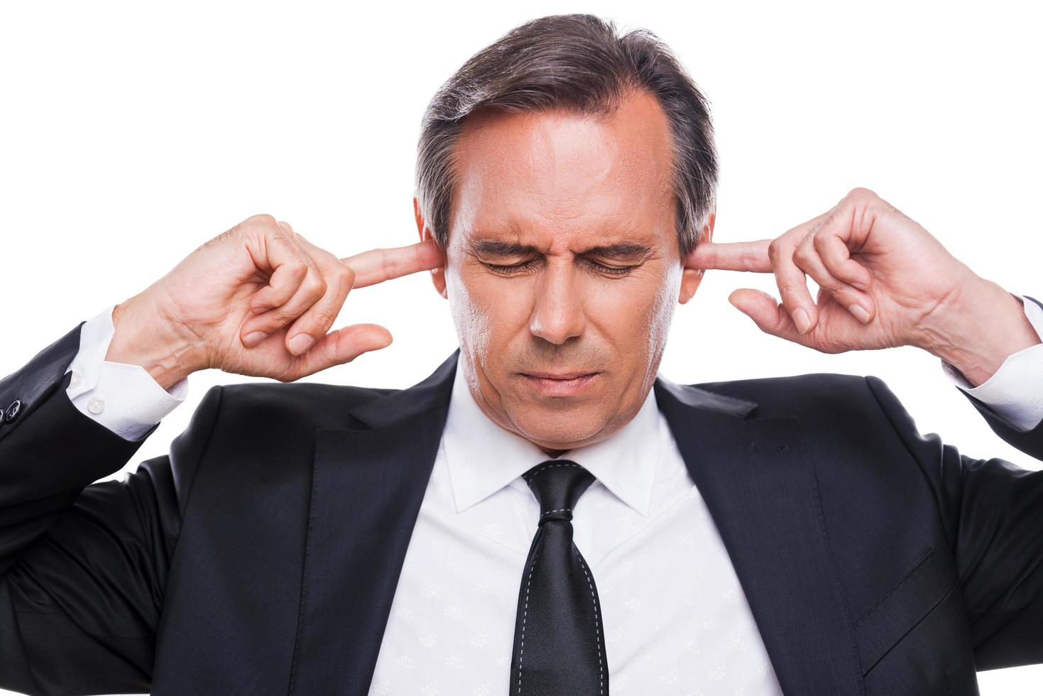 Too loud sound. Confident mature man in shirt and tie holding fingers in ears and keeping eyes closed while standing isolated on white background photo