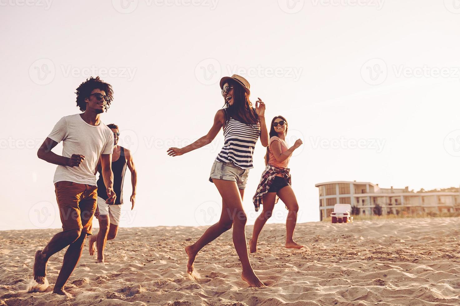 Young and free. Group of young cheerful people running along the beach and looking happy photo
