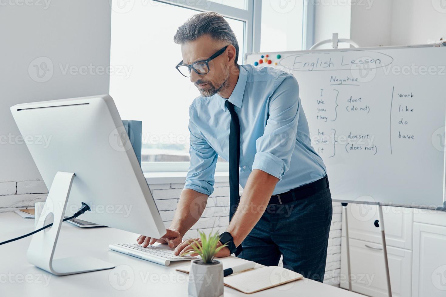 Confident English teacher using computer while standing near the