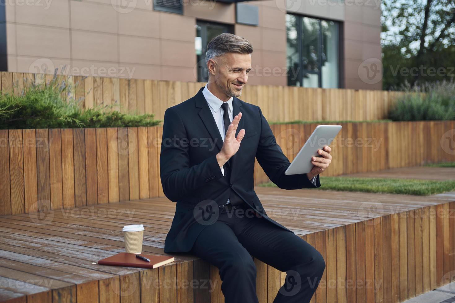 Confident mature businessman using digital tablet while sitting outdoors near office building photo