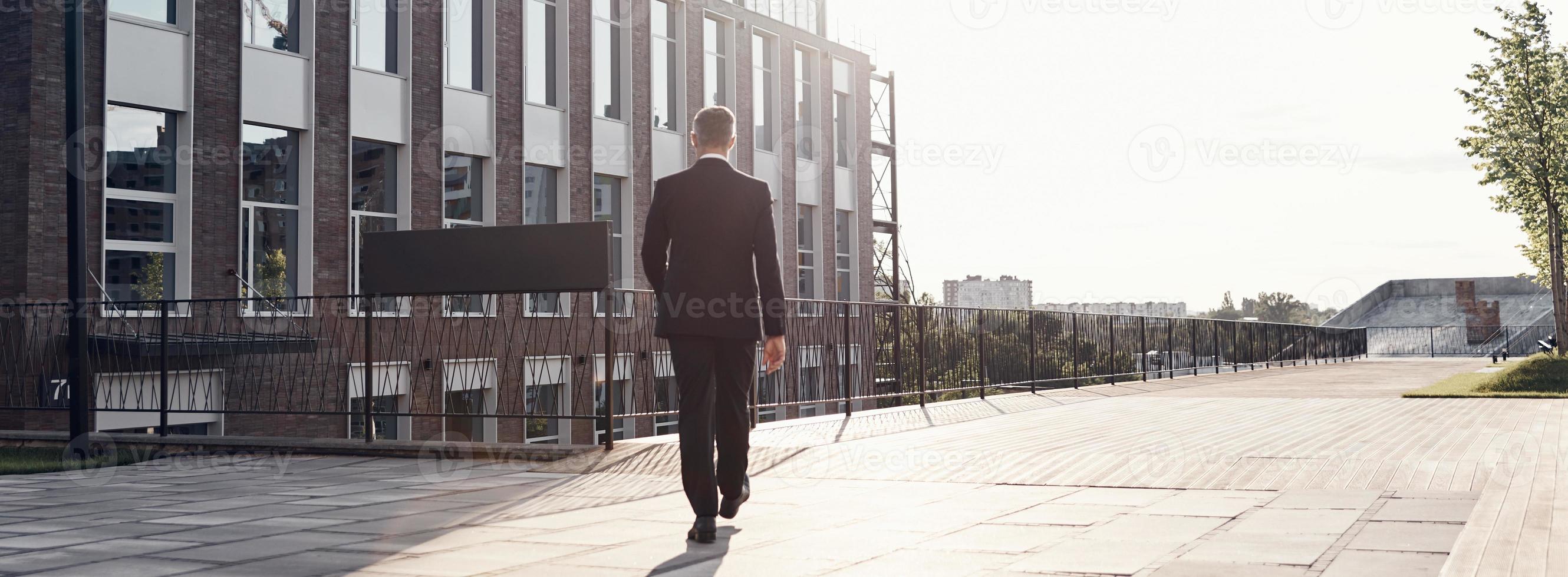 Full length rear view of man in full suit walking near office building outdoors photo