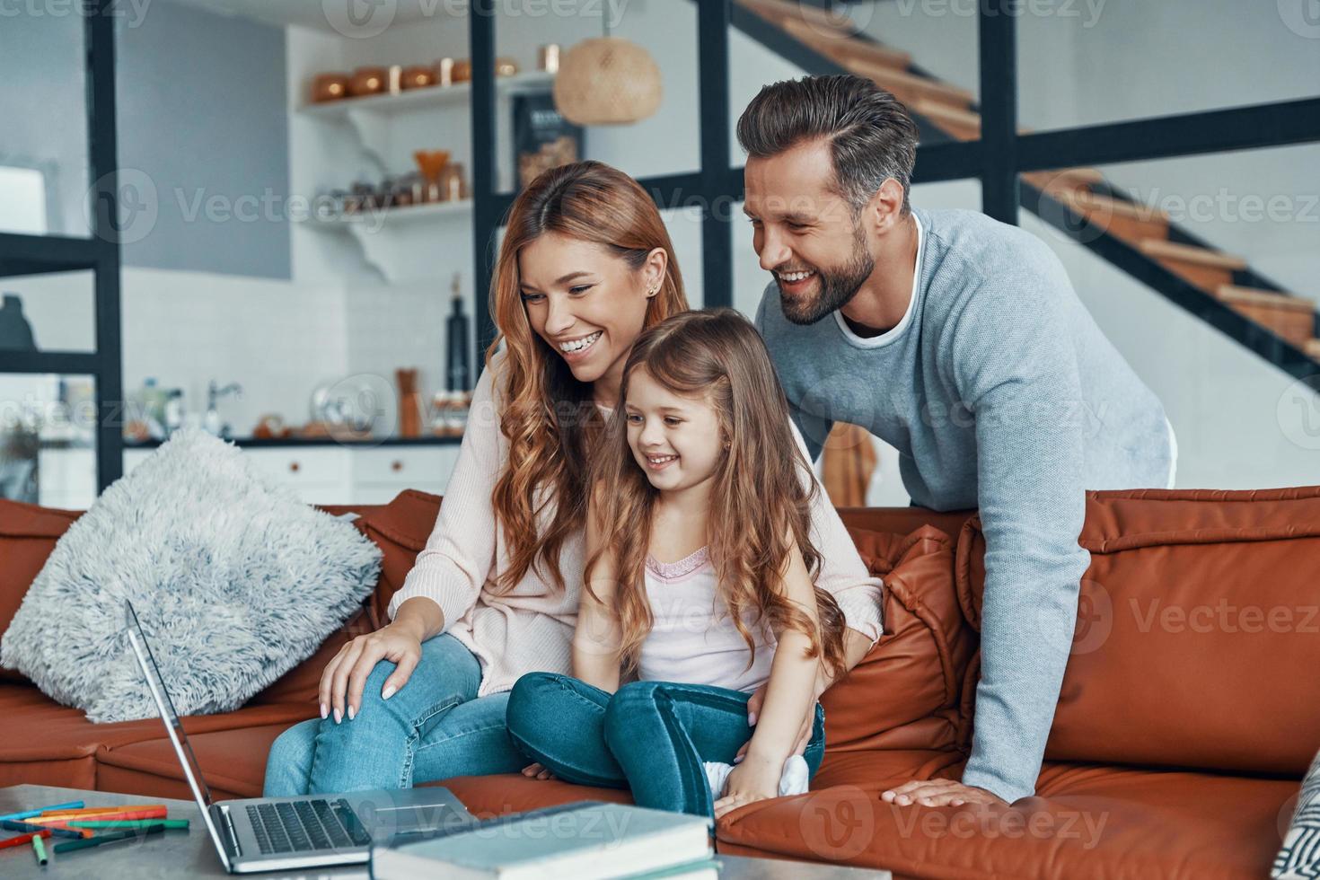 Playful beautiful family with little girl bonding together and smiling while using laptop at home photo