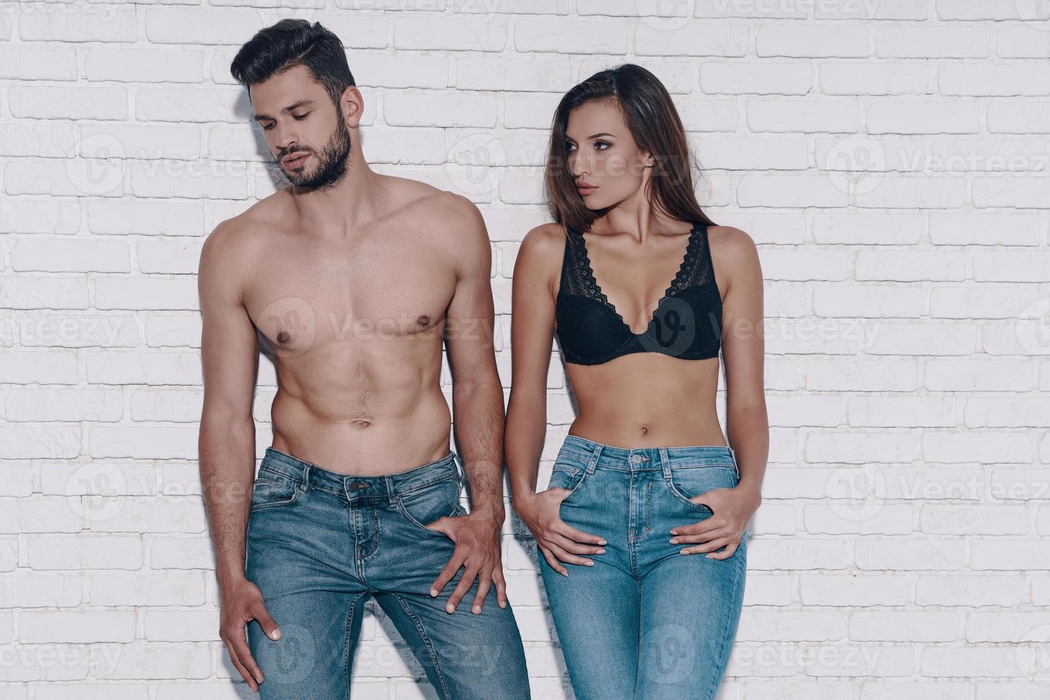 Stylish couple. Beautiful young couple looking away while standing against brick wall photo