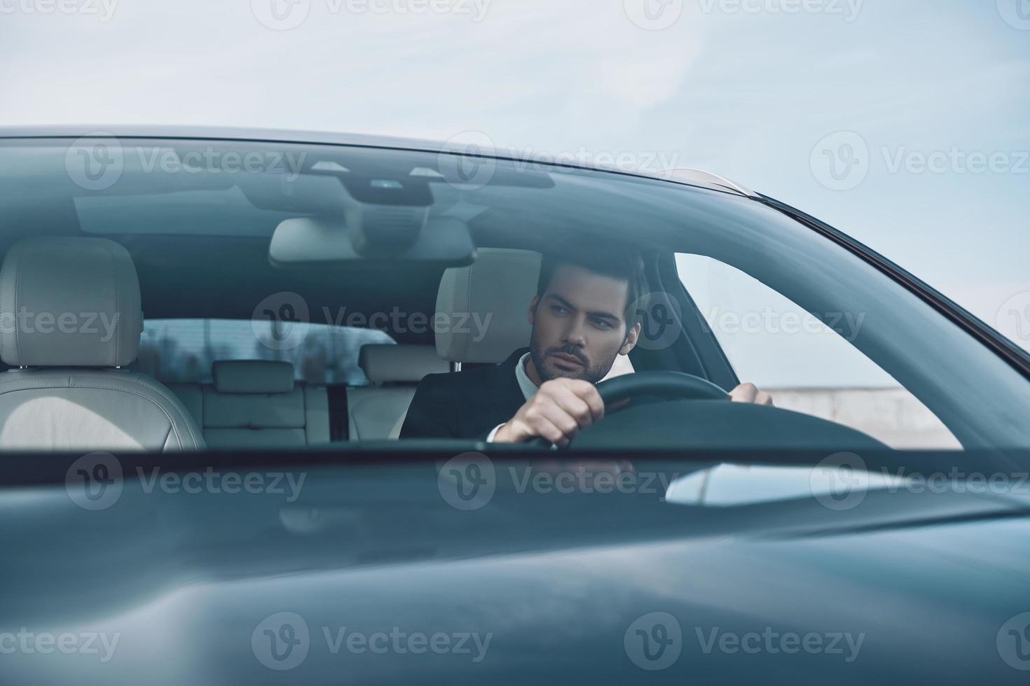Concentrating on the road. Handsome young man in full suit looking straight while driving a car photo