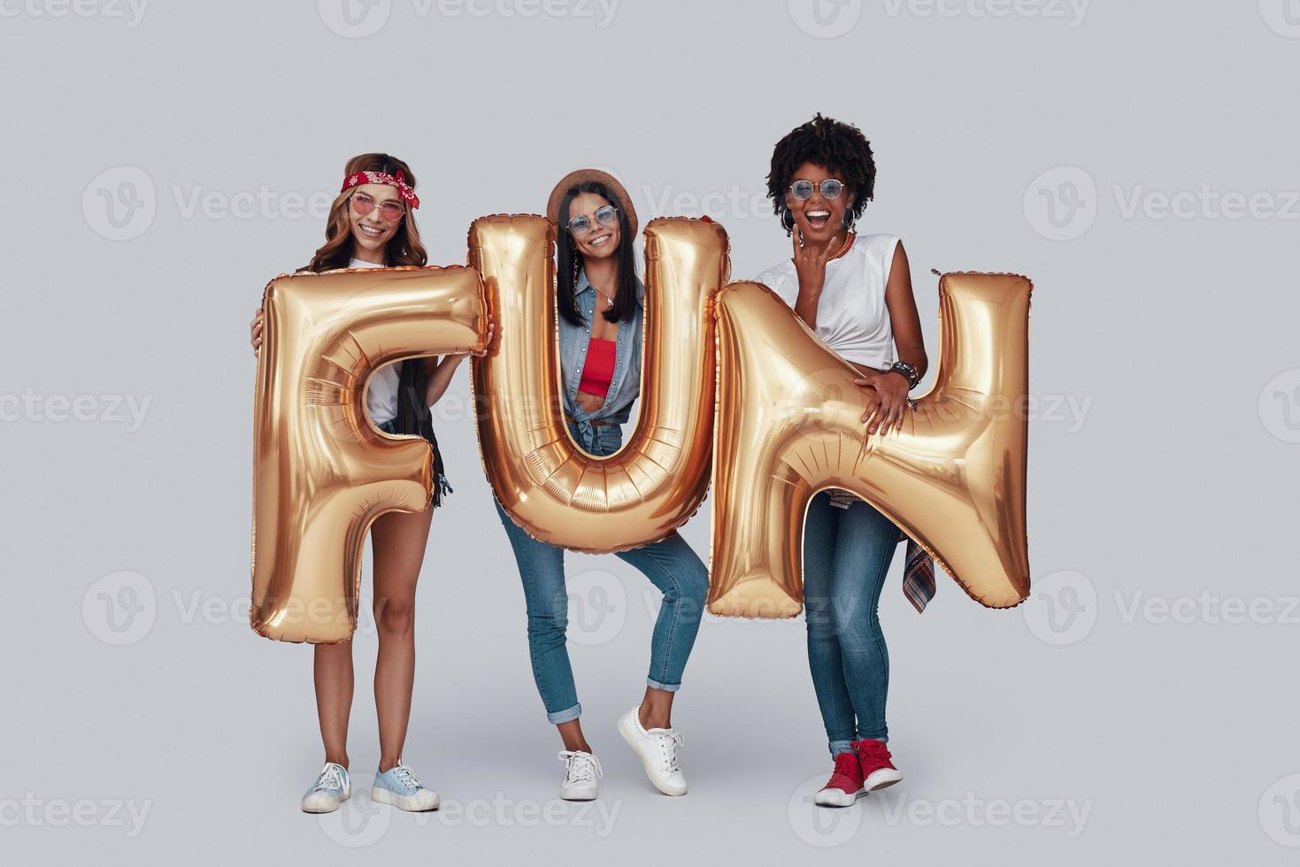 longitud total de tres mujeres jóvenes atractivas que llevan globos y sonríen mientras están de pie contra el fondo gris foto