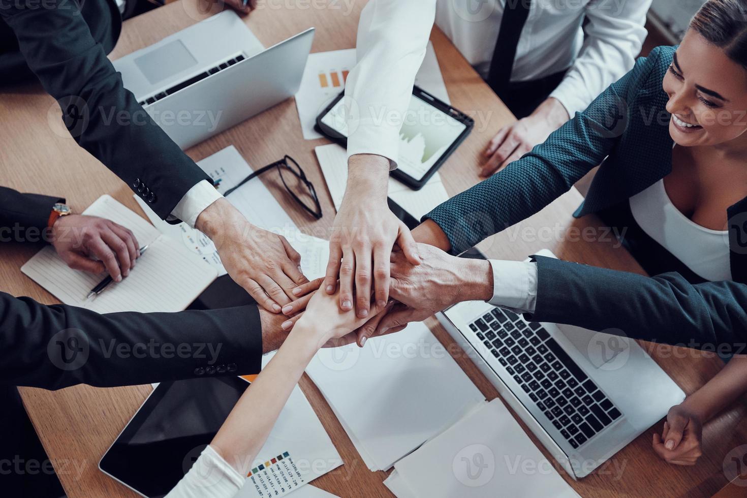 Top view of cheerful business team keeping hands together as a symbol of unity while working together in the modern office photo