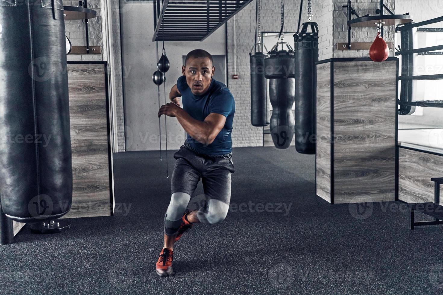 Pushing himself to the limit. Full length of handsome young African man in sport clothing running while exercising in the gym photo