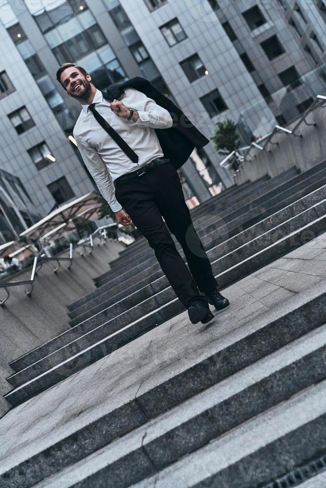 confiado y guapo. toda la longitud de un joven con traje completo sonriendo mientras camina al aire libre foto