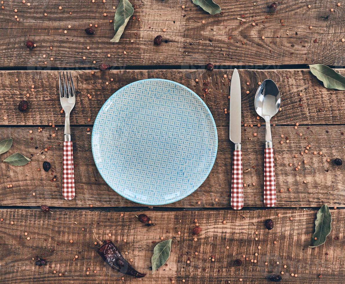 Time for dinner High angle shot of empty plate, fork, spoon, knife lying on rustic table photo