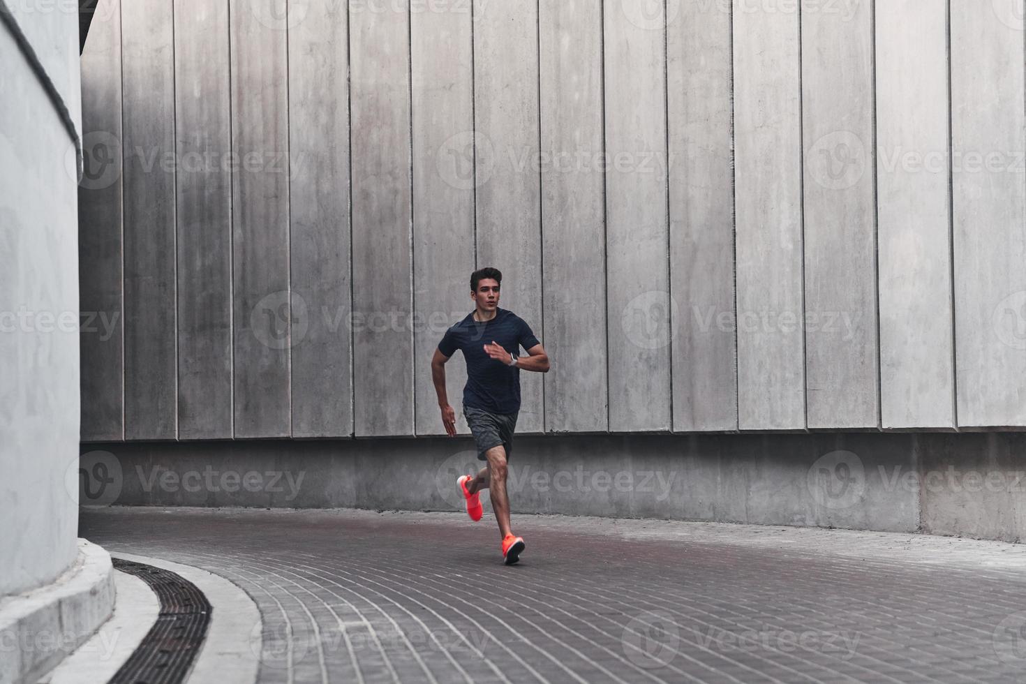 Morning workout. Full length of young man in sports clothing running while exercising outside photo